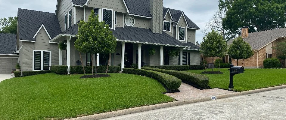 House in Kingwood, TX, with a lawn, trimmed shrubs, and small trees.