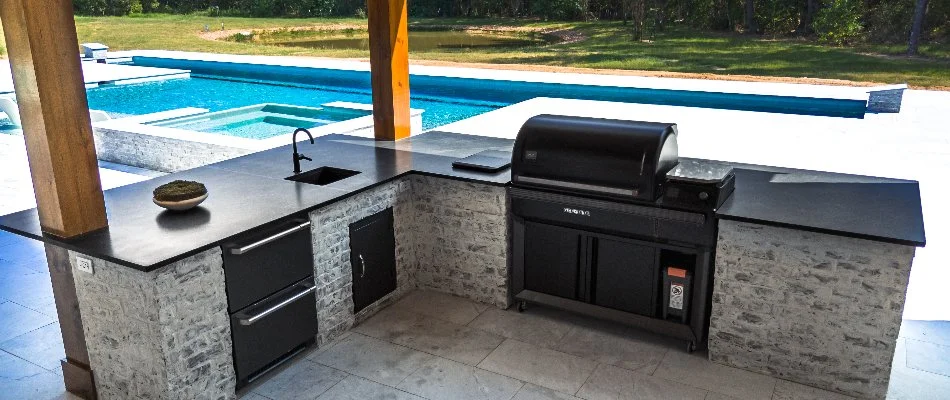 Outdoor kitchen on a patio in Kingwood, TX, with a pool in back.